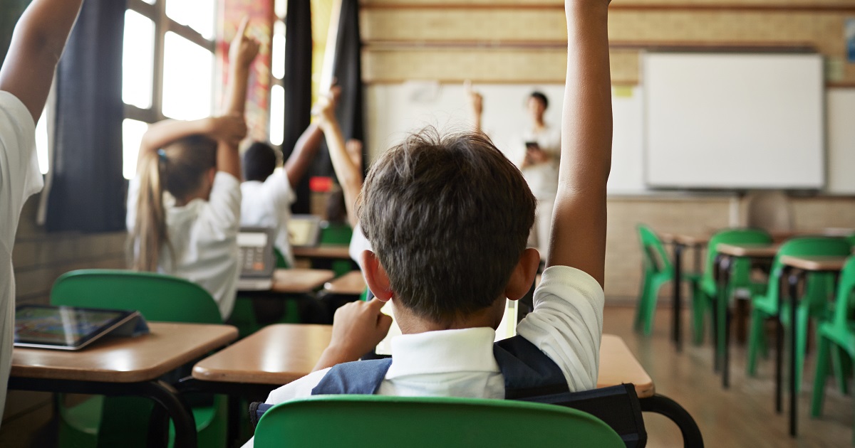 Student in classroom desk raising hand