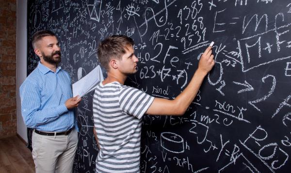 Teacher and student writing on big blackboard with mathematical calculations