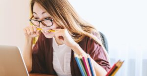 Female online student chewing her pencil looking at laptop
