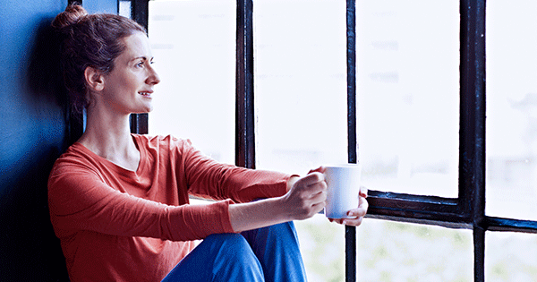 Woman relaxing with a cup of coffee, staring out the window, being mindful.