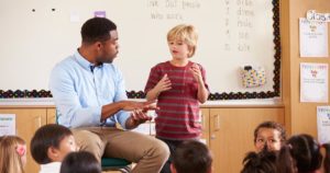 Teacher talking to kid standing in front of class