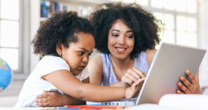 Woman helping child read on a laptop