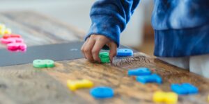 Kid picking up numbered tiles from a wooden table