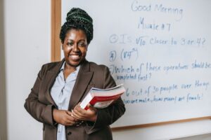 Teacher standing in front of whiteboard carrying books