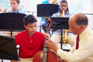 Boy learning to play cello in high school orchestra