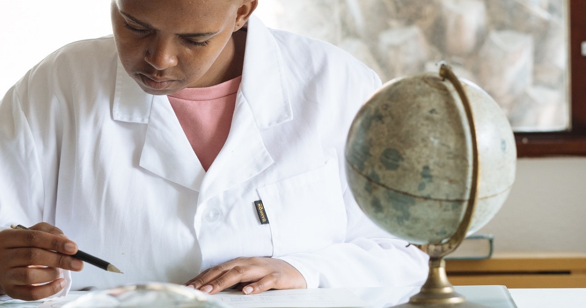 Woman writing at her desk with globe in foreground on desk